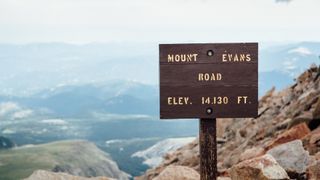 A sign on Mount Evans shows the elevation with mountains in the background