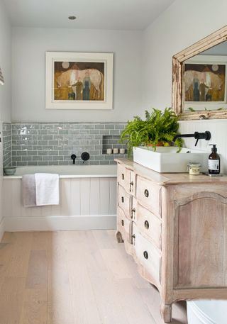 bathroom with tongue and groove panel on bath pale blue walls and tiles pale wood effect floor and stripped antique cabinet used as vanity unit