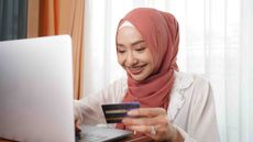 Photo of a smiling woman looking at a computer screen holding a credit card