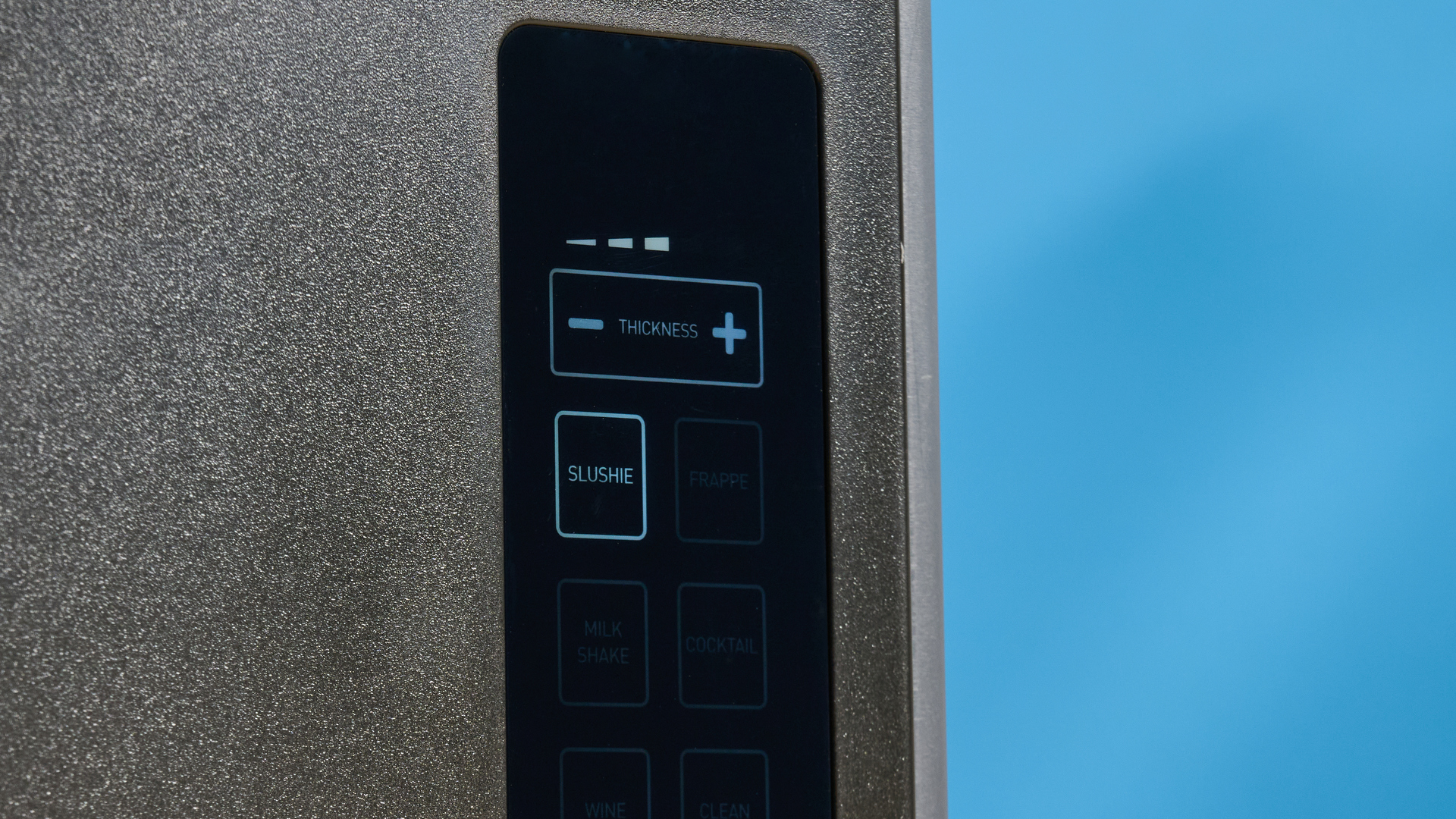 the inoviva slushie machine, a slushie maker with a plastic cylinder body, a dispensing spout, photographed making orange juice slush against a blue tom&#039;s guide background