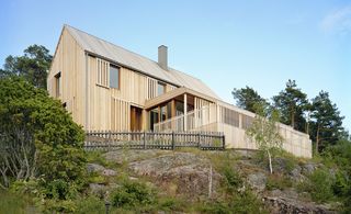 Villa Arkö sits on rocky terrain, surrounded by trees. The façade is made out of light wood.