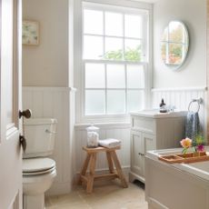 Neutral traditional bathroom, with wall panelling, sash window and wooden stool