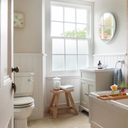 Neutral traditional bathroom, with wall panelling, sash window and wooden stool