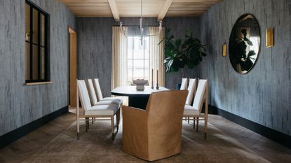 Image of a formal light blue dining room, there is a black, oval table with six white, cushioned chairs around the table and a leather seat at the head.