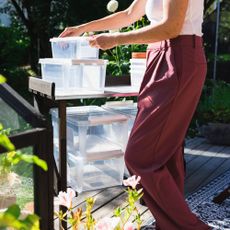 A woman's. hands placing plastic storage bins on a cart outdoors surrounded by plants