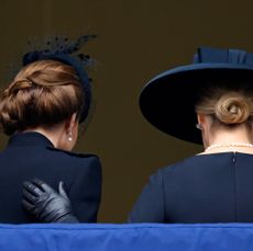 The back of Kate Middleton and Duchess Sophie wearing black coats and black hats as Sophie puts a gloved hand on Kate's back