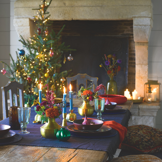 Living room with a decorated and lit Christmas tree beside a fireplace with lit candles on a table in the foreground.