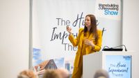 woman in a yellow suit speaking on a stage at the Homebuilding & Renovating Show