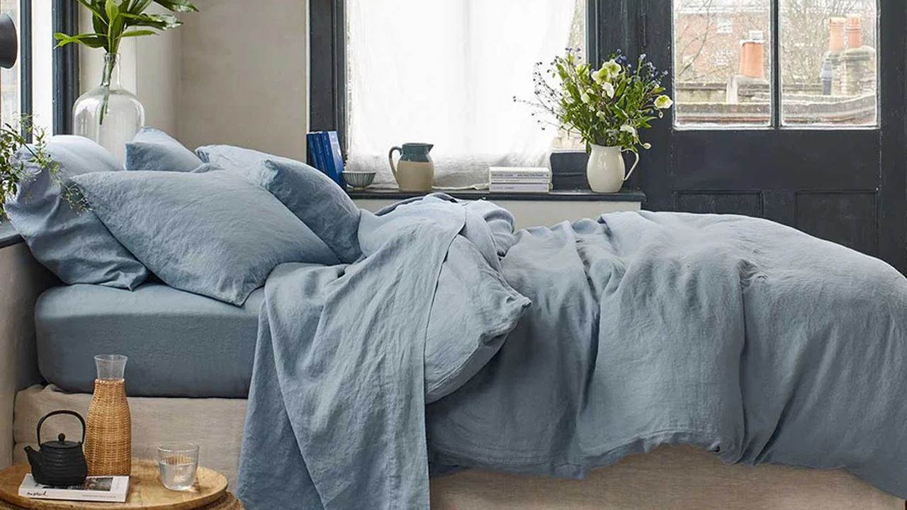 A bedroom with large black-framed windows and a bed dressed with a muted blue linen duvet cover and pillows