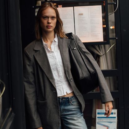 a guest attends paris spring summer 2025 fashion week in a grey blazer black handbag and white button down shirt 