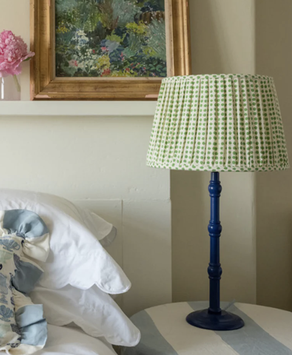 a pleated green patterned lampshade on a blue base next to a bed