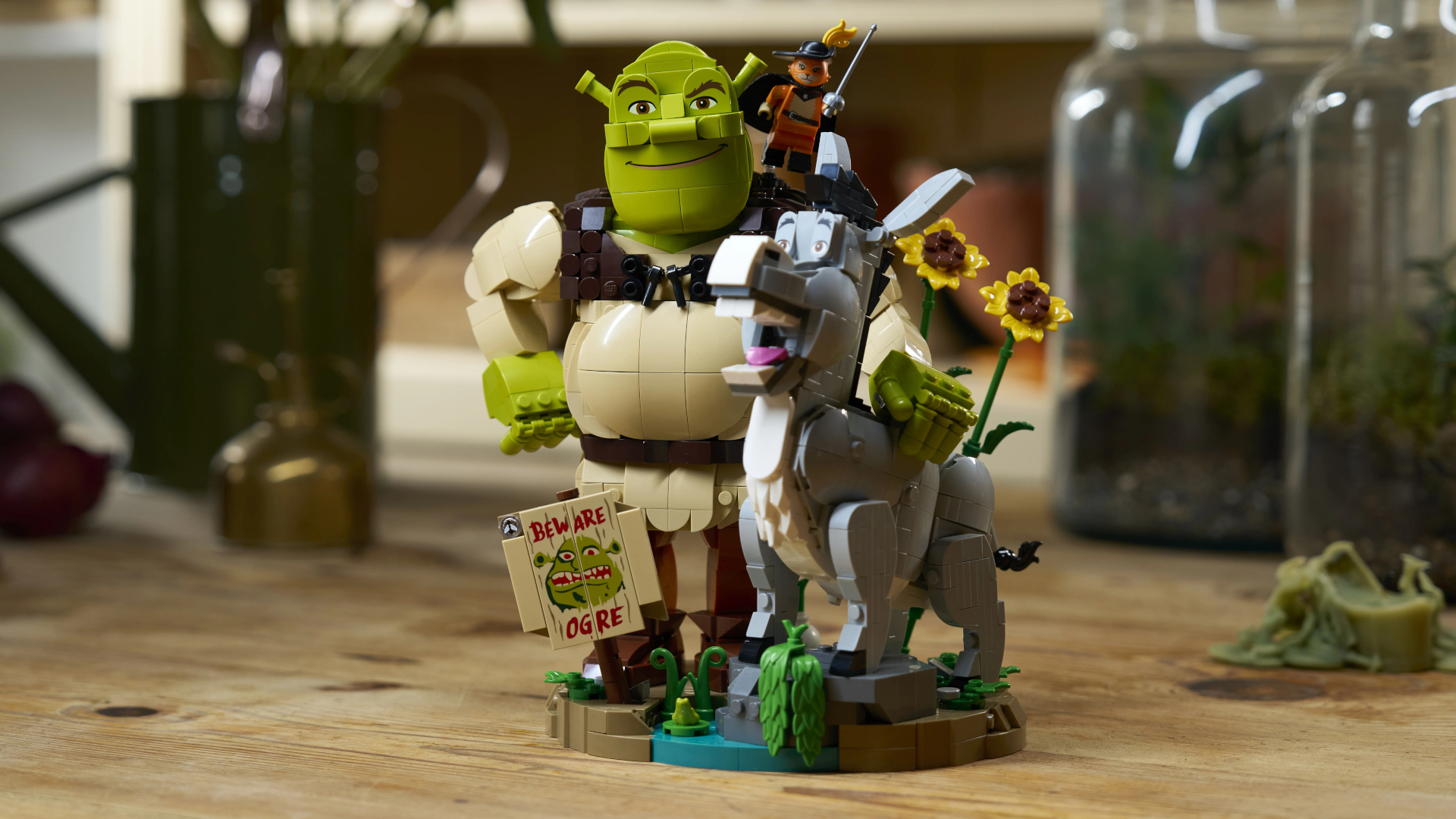 Lego Shrek, Donkey, and Puss in Boots set on a wooden table with jars visible behind