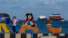 A woman poses in front of a sign welcoming visitors to Maracaibo, with an oil tanker in the background