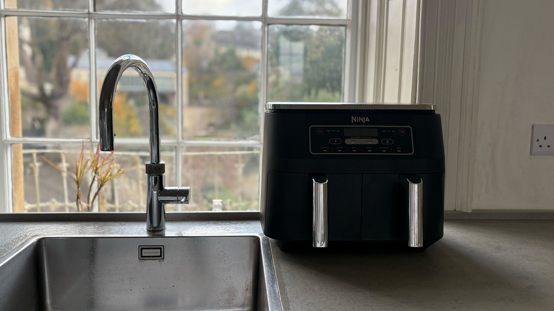 kitchen sink with a window behind and an air fryer placed too close on the countertop