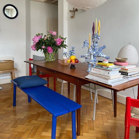 a table with a blue bench red chairs and white bench is pictured with magazines, books, candles, and flowers on top of it