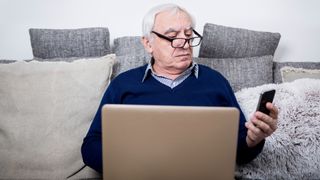 old man looking at phone while on laptop
