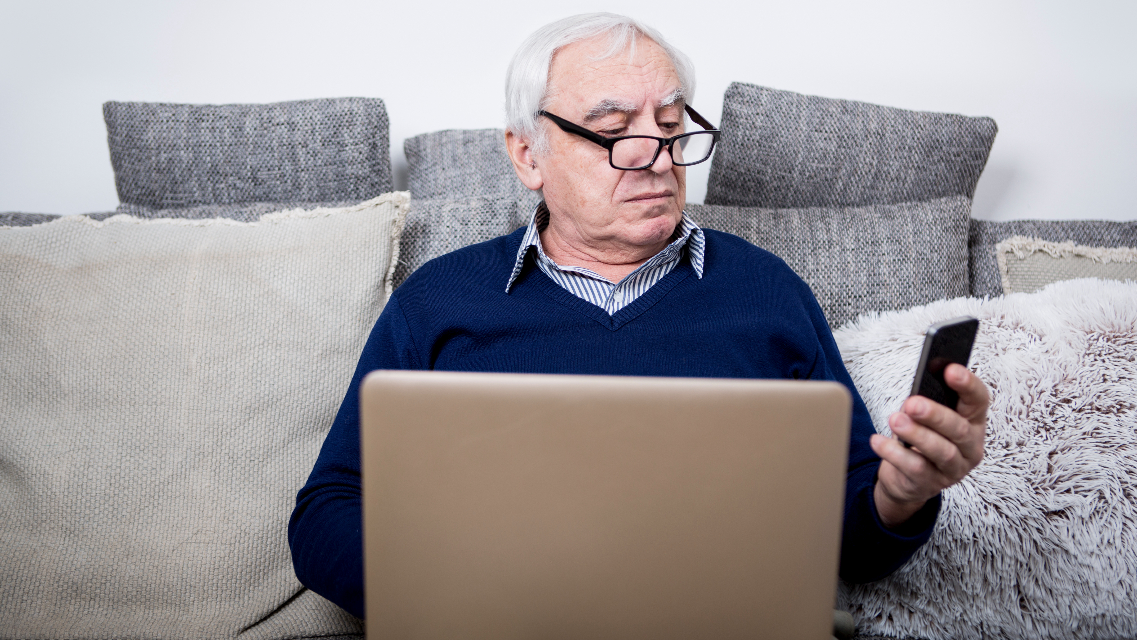 old man looking at phone while on laptop