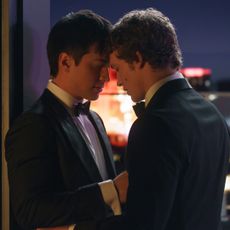 Two men (Hudson Williams as Shane Hollander and Connor Storrie as Ilya Rozanov) stand closely in front of a city skyline at night, in the TV show 'Heated Rivalry.'