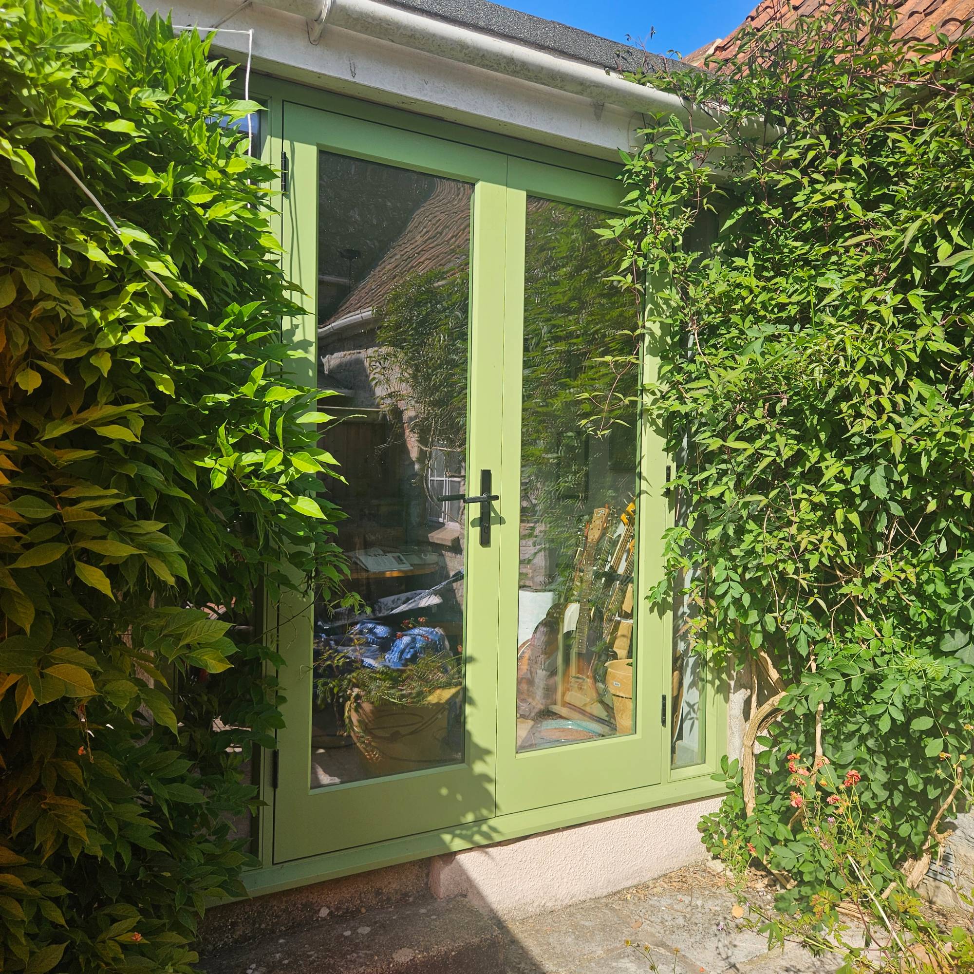 green timber patio doors with black handles and established planting