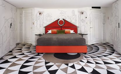 Hotel room with red bed, patterned carpets and white walls with images drawn on them