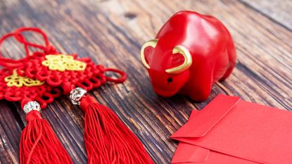 A Chinese New Year display of a red ceramic ox, red tassels and red envelops.