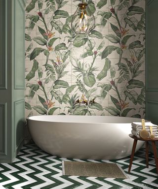 Bathroom with jungle design wall tiles and dark green and white subway tiles on floor in zig-zag formation, with white contemporary freestanding tub