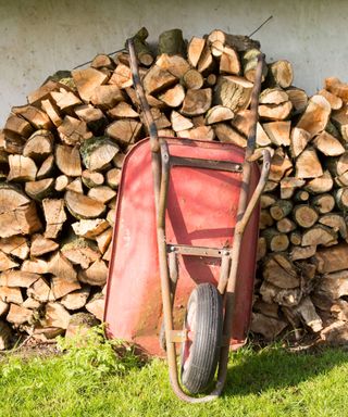 A log pile with a red wheelbarrow leant against it