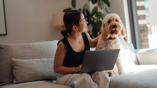 Woman sitting on a couch with a laptop and her dog next to her