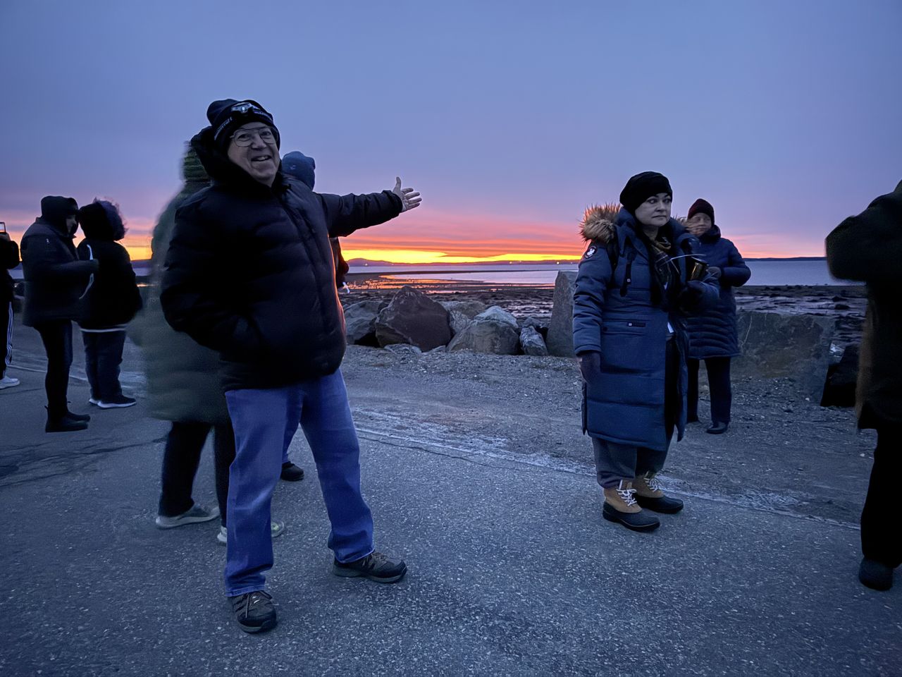 A man smiles and holds out his arm in the direction of the rising sun.