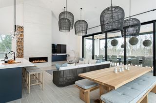 living room coastal modern with navy blue kitchen cabinets in the open space plus black fixtures, bench dining table and black rattan L-shape couch