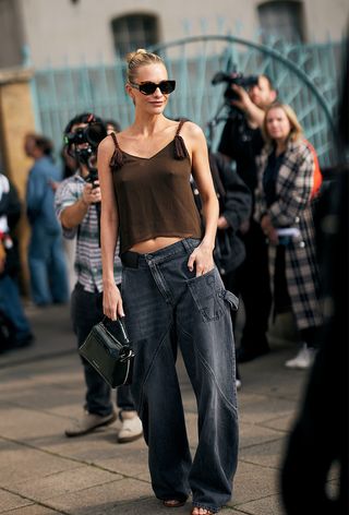 foto gaya jalanan Poppy Delevingne mengenakan tank top cokelat dan celana jins hitam untuk pertunjukan musim semi JW Anderson 2025