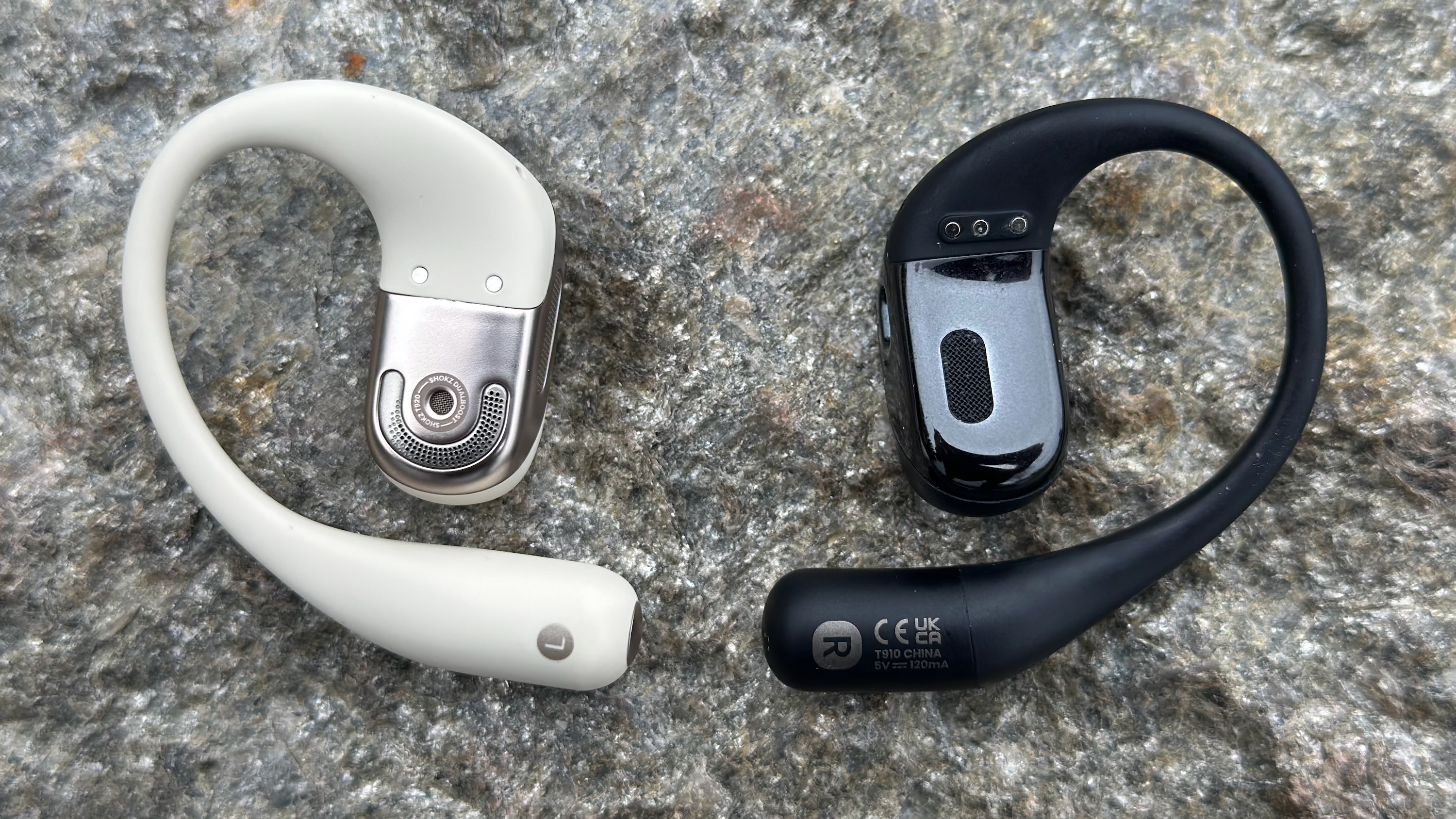 The white Shokz OpenFit 2 and black Shokz OpenFit sitting aside one another, showing the larger speaker grille on the newer model, as well as the redesigned ear hook.