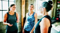 Three women standing in a gym talking