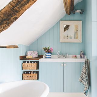 coastal bathroom with blue painted tongue and groove, beams, white ceiling, floor and bath, striped towels, storage baskets