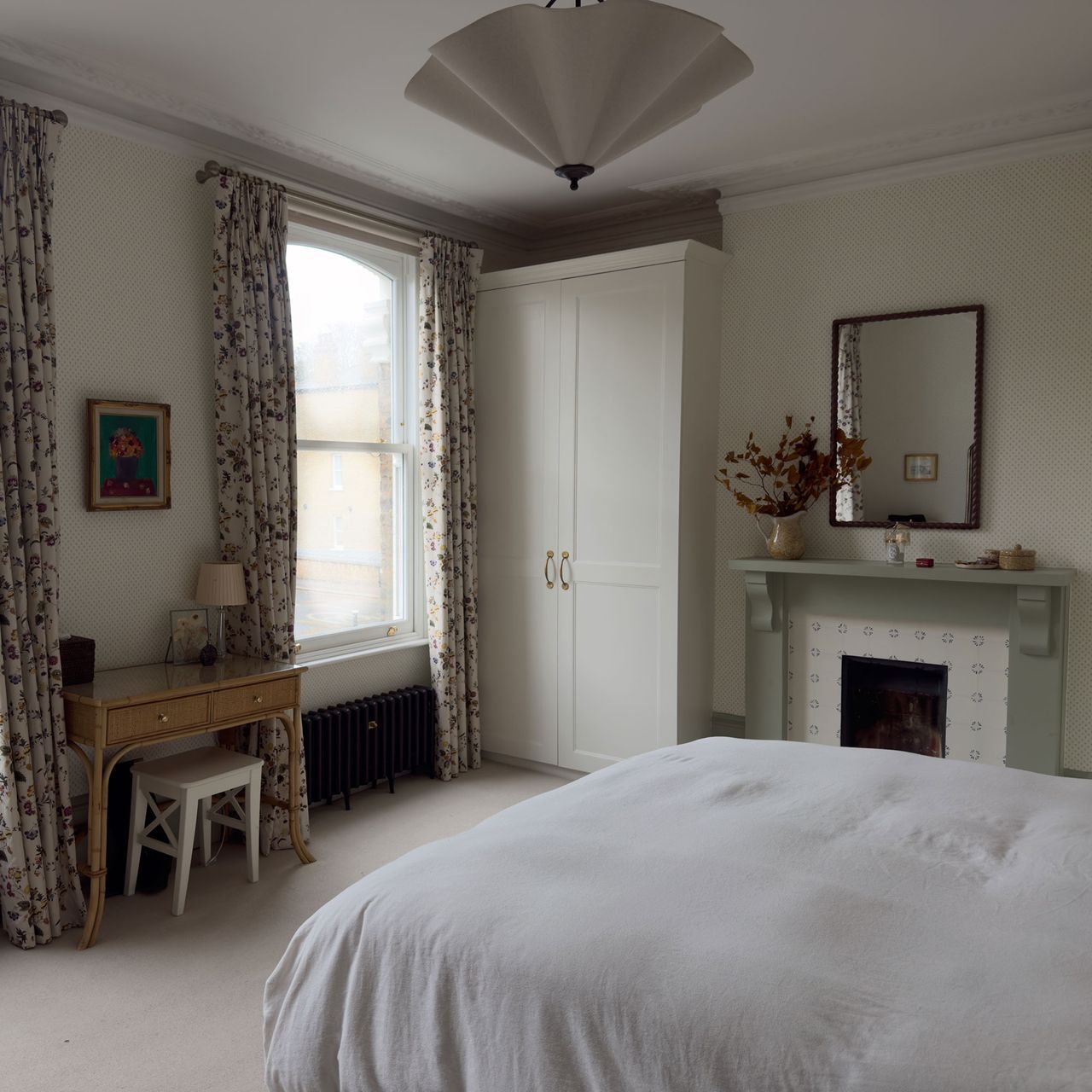 Neutral bedroom with fireplace, wooden vanity and floral curtains