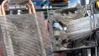 A dusty heatsink and fan being cleaned by a brush