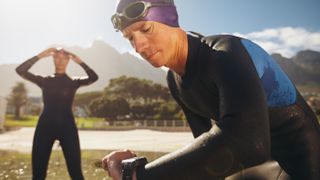 Man wearing wetsuit by a lake checking his sports watch