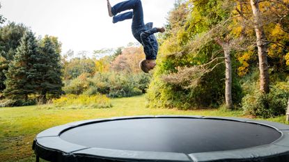 A child jumping on an inground trampoline in yard