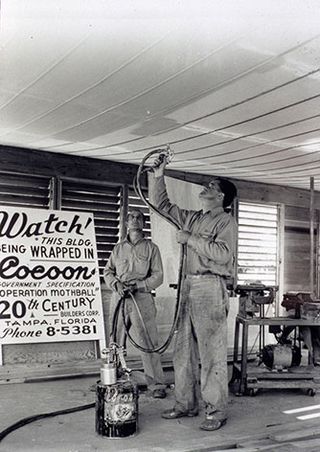 A black and white photo of two males spraying a ceiling.
