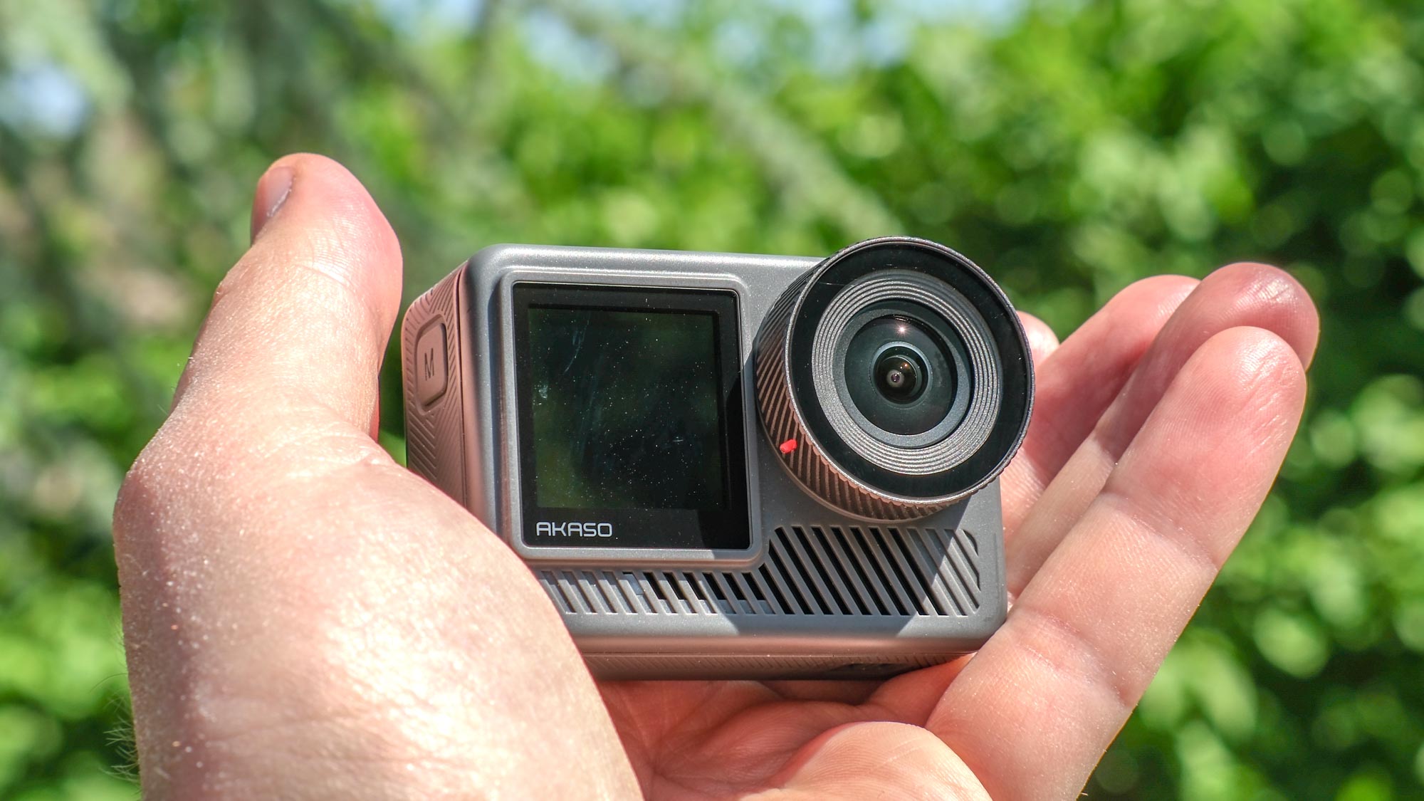 A photo of the Akaso Brave 8 Lite in hand against a green, out of focus background.