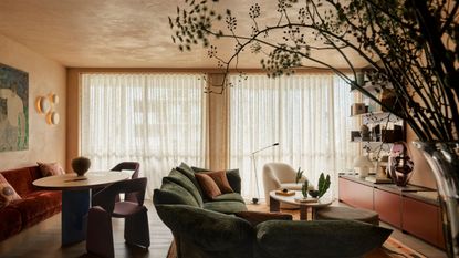 modern living room with plaster walls and ceiling, sheer curtains, green edra standard sofa, red console under TV, round timber dining table with red banquette seating