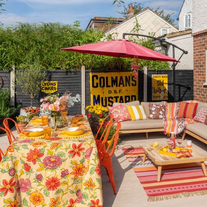 Patio with beige outdoor corner sofa, pink umbrella, orange garden chairs and floral table cloth