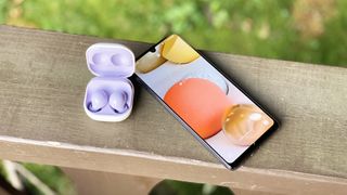 Samsung Galaxy Buds 2 i sitt laddningsfodral bredvid en mobil.