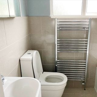 A small bathroom with white toilet sanitaryware, greige gloss wall tiles, and metal heated towel rail