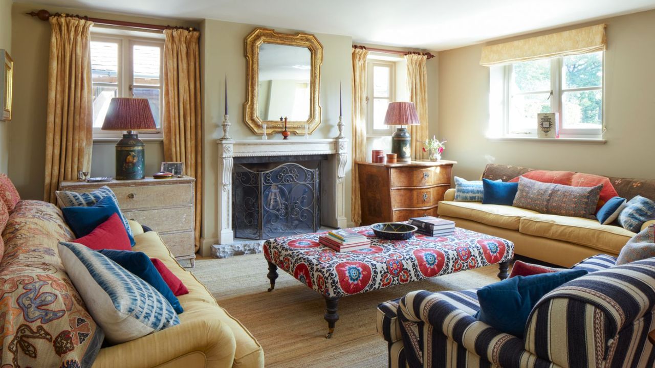 Cozy living room with matching yellow sofas, striped armchair, surrounding a patterned ottoman and fireplace