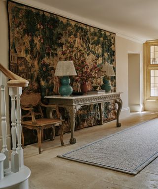 light and bright entryway decorated in a vintage style with a large wall hung tapestry and a entry table styled with two matching green table lamps