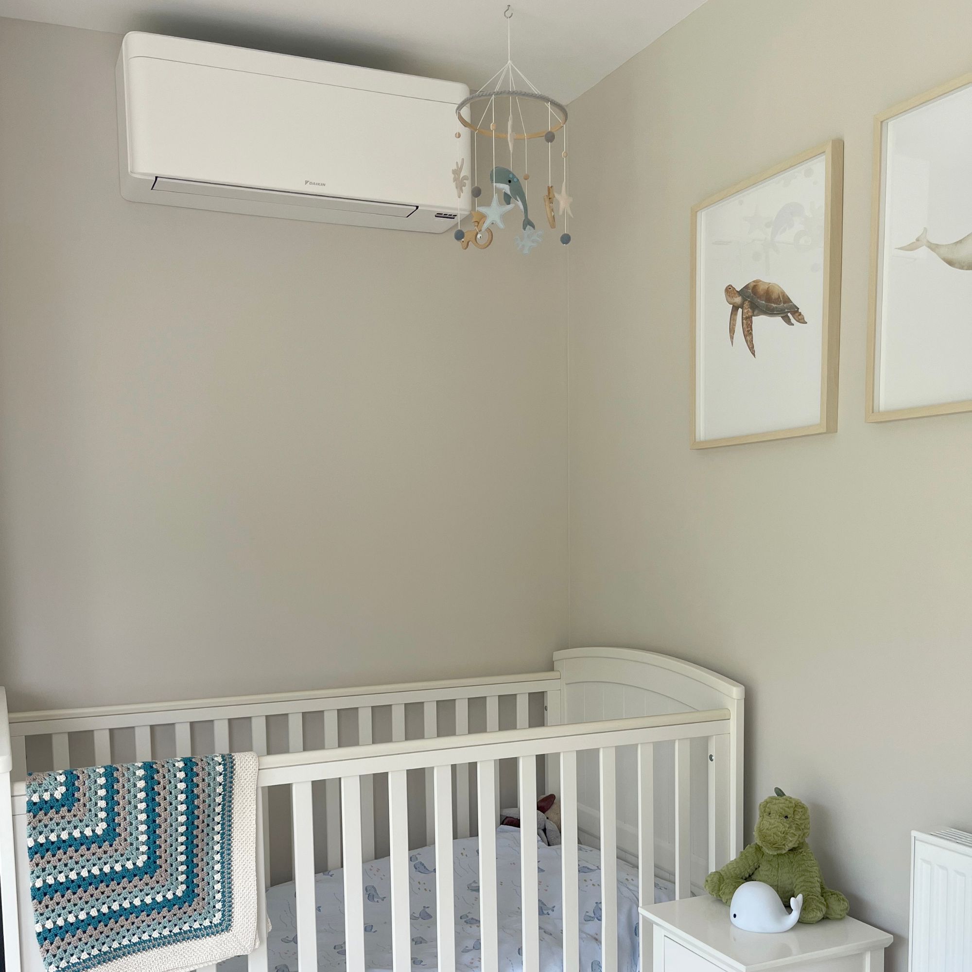 Fitted air conditioning unit on a neutral wall above a cot in a nursery