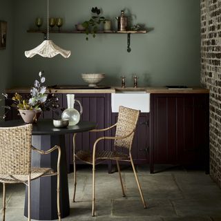 kitchen with wickers chairs, dining table, dark purple cabinets, wooden shelving and green walls