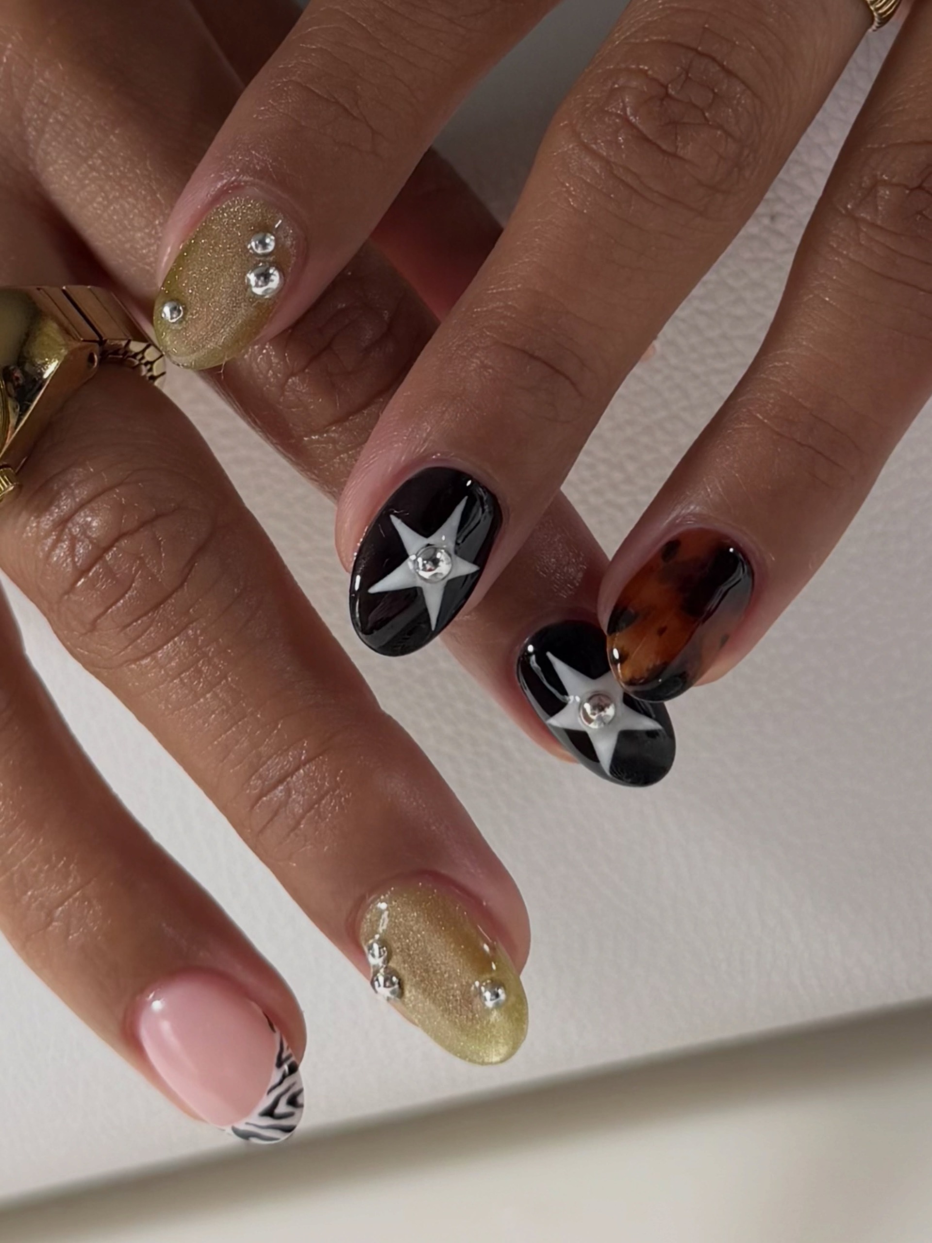 Close-up of a mixed manicure with gold glitter, black-and-white star designs, tortoiseshell accents, and rhinestones