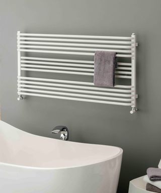 white horizontal towel rail radiator on grey wall with bath below